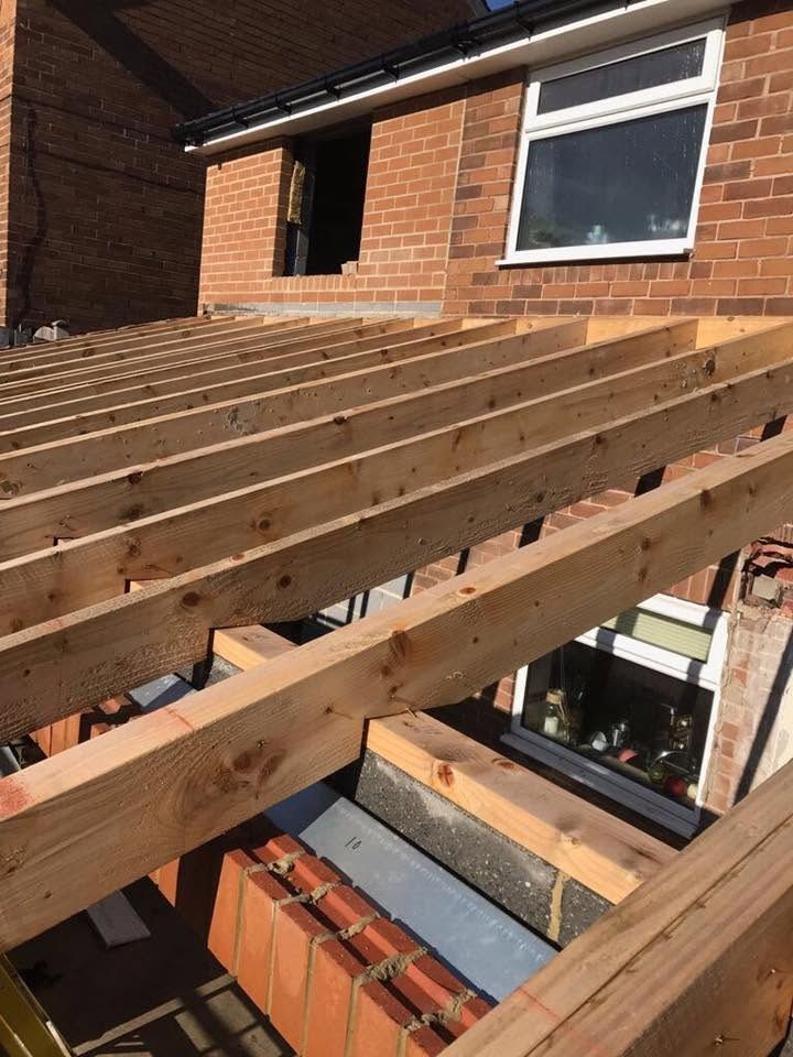 New treated timber joists spanning an extension in low sunlight, bedded on red brick walls with a concrete lintel