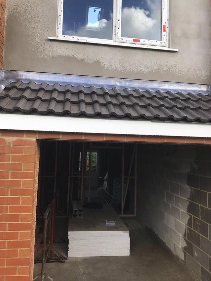 Charcoal double roman tiles and new lead apron flashing over an extension, with timber studwork and blockwork visible in the opening below