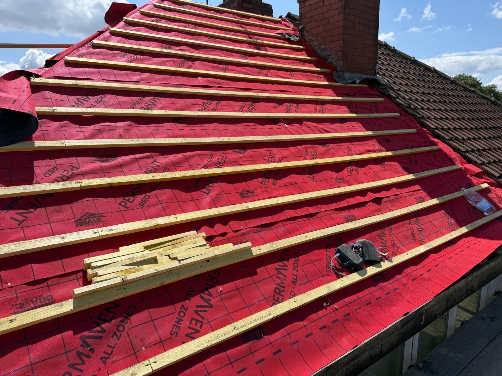 Full hipped roof slope covered in red breathable membrane with new battens, and a brick chimney stack finished with fresh lead flashing
