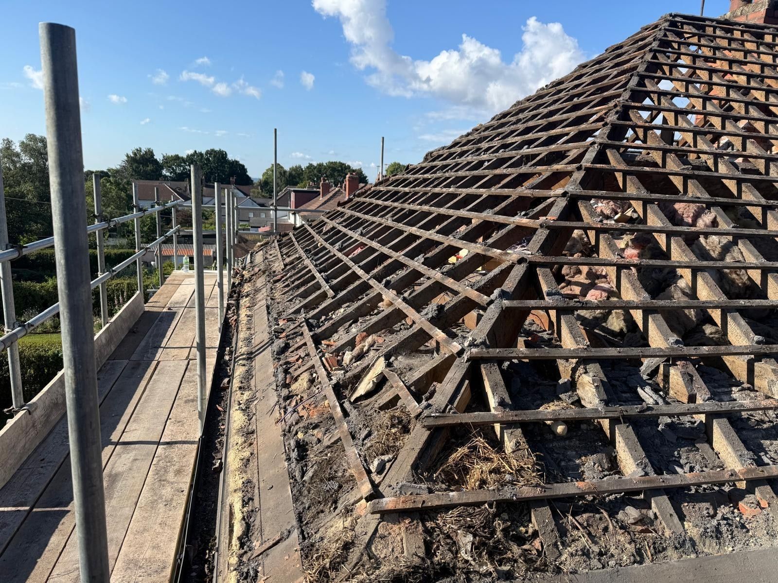 Roof stripped back to bare rafters and old laths during a full re-roof, with scaffold edge protection in place