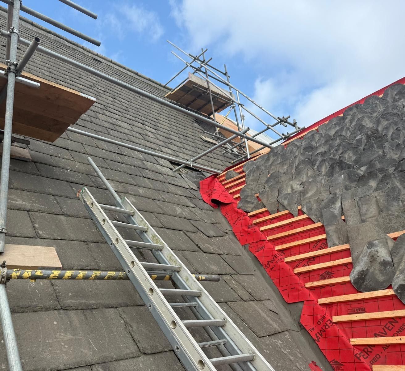 Heritage roof slope part way through re-slating, old stone slates on one side and new battens with slates being laid on the other